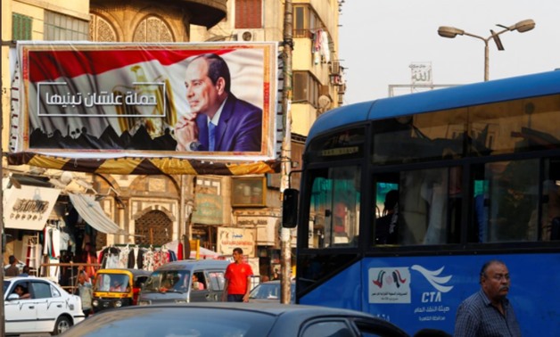 People walk near a poster of Egyptian President Abdel Fatah al-Sisi of the campaign titled, “Alashan Tabneeha” (So You Can Build It), at Sayeda Zainab square in downtown of Cairo, Egypt