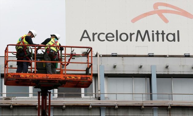 Workers stand near the logo of ArcelorMittal, the world's largest producer of steel, at the steel plant in Ghent, Belgium, July 7, 2016 - REUTERS/Francois Lenoir