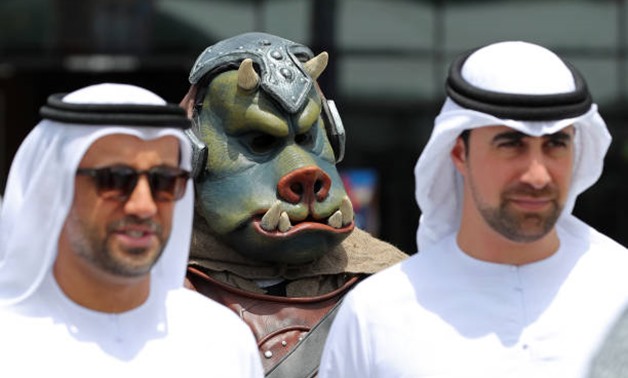A cosplayer poses for a photograph behind two men at the Middle East Film and Comic Con on April 5, 2018 in Dubai
