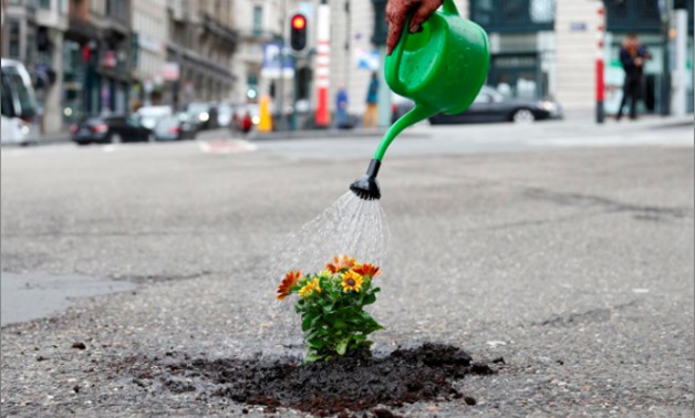 Brussels resident Anton Schuurmans waters flowers after planting them in an unrepaired pothole to draw attention to the bad state of public roads in Brussels, Belgium April 5, 2018. REUTERS/Francois Lenoir