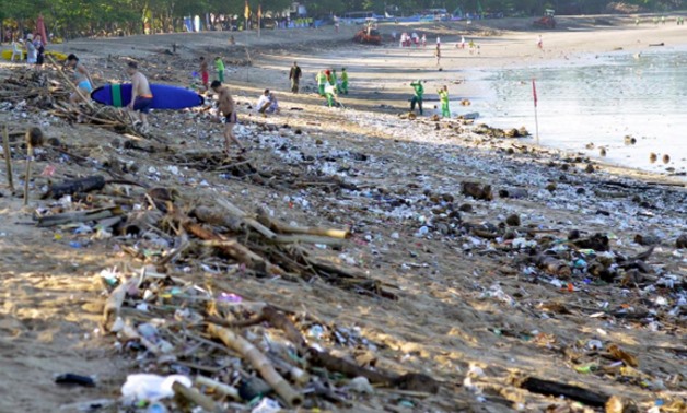 FILE PHOTO: Tourists walk amongst trash washed up on Kuta beach by seasonal winds, as workers attempt a clean-up in the background, on the Indonesian island of Bali February 15, 2016 in this photo taken by Antara Foto. REUTERS/Wira Suryantala/Antara Foto
