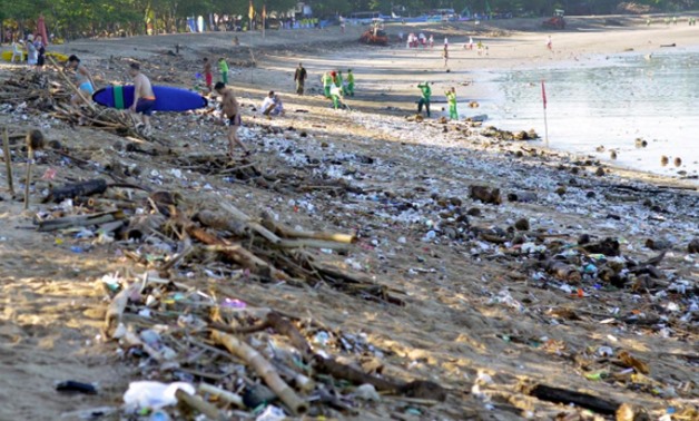 FILE PHOTO: Tourists walk amongst trash washed up on Kuta beach by seasonal winds, as workers attempt a clean-up in the background, on the Indonesian island of Bali February 15, 2016 in this photo taken by Antara Foto. REUTERS/Wira Suryantala/Antara Foto