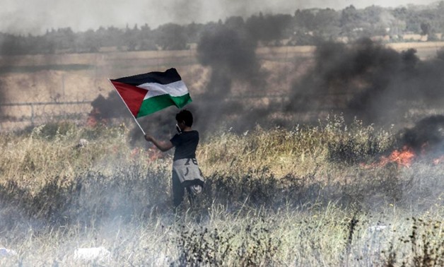 A Palestinian boy holds his national flag during clashes with Israeli security forces on the Gaza-Israel border on April 6, 2018
