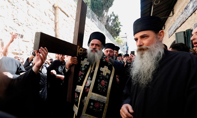 A Greek Orthodox bishop carries a large wooden cross with fellow worshippers along the Via Dolorosa (Way of Suffering) during the Orthodox Good Friday procession in Jerusalem's Old City on April 6, 2018. / AFP / GALI TIBBON