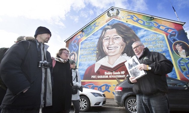 Coiste guide Peadar Whelan (right) talks to his group of tourists in front of a mural to of IRA hunger striker Bobby Sands during a political guided tour in west Belfast March 27, 2018. — AFP pic