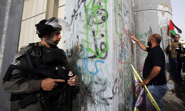 An Israeli solider watches as a Palestinian uses a spray can to draw a graffiti on Israel's controversial separation barrier - AFP