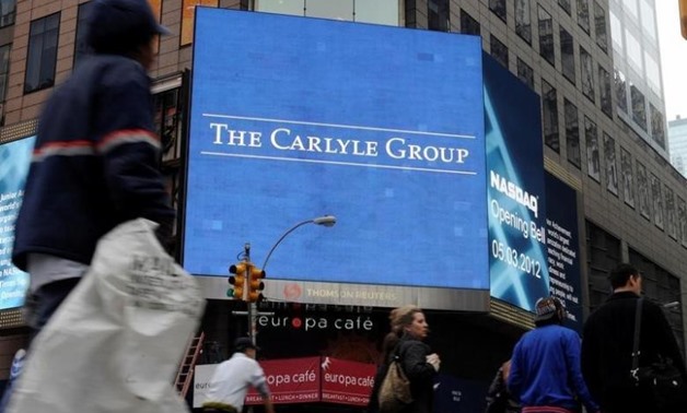 FILE PHOTO: Passersby walk in front of video monitors announcing the Carlyle Group's listing on the NASDAQ market site in New York's Times Square after the opening bell for trading, U.S. May 3, 2012. REUTERS/Keith Bedford/File Photo