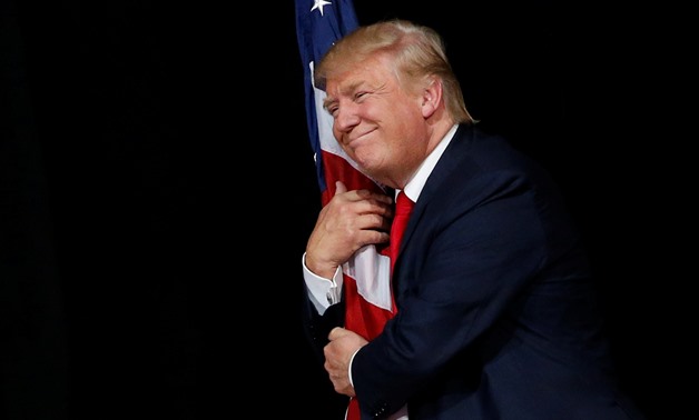 U.S. president Donald Trump hugs a U.S. flag as he comes onstage to rally with supporters in Tampa, Fla., on October 24, 2016. — Reuters

