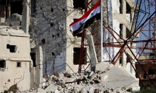 The Syrian national flag flies among damaged buildings in an opposition-held part of the southern city of Daraa on July 12, 2018 - AFP