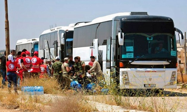 In this photo released by the Syrian official news agency SANA, Syrian government forces and Syrian Arab Red Crescent oversee the evacuation by buses of opposition fighters and their families from the southern province of Daraa, Syria, Sunday, July 15, 20