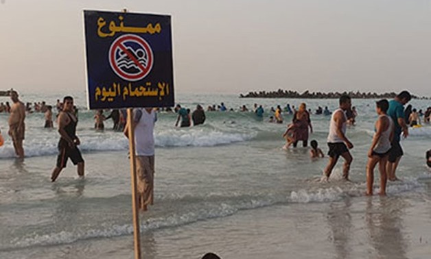 Caption: FILE - Holidaymakers swim beside a sign that says “No swimming” - Egypt Today