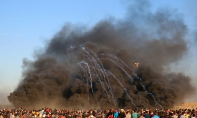 © AFP/File | Palestinians protest along the Israel-Gaza border on September 14, 2018 as Israeli forces fire tear gas canisters through smoke from burning tyres