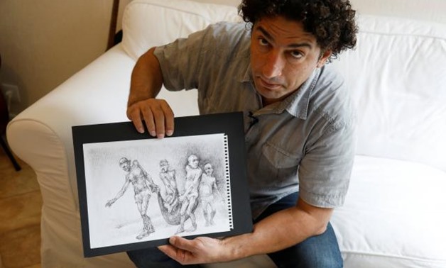 Exiled Syrian artist Najah al-Bukai poses with a ball-pen drawing that stems from the haunting memories of the torture Bukai says he went through and witnessed when imprisoned twice in Syrian government jails, in Yerres, near Paris, France, September 13, 