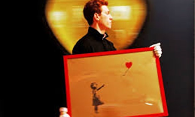 FILE PHOTO: An employee walks with Banksy’s “Girl and Balloon” 2009, at Bonhams auction house in London March 23, 2012, REURERS/LUKE MacGregor/File Photo