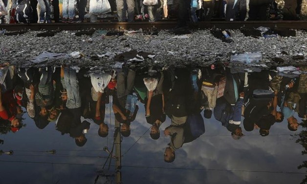 Syrian refugees are reflected in a puddle as they wait for their turn to enter Macedonia at Greece's border. (photo credit: REUTERS)