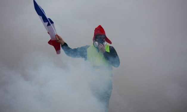 © AFP | A demonstrator holds a French flag as they walk amid the tear gas during a protest of Yellow Vests (Gilets jaunes) against rising oil prices and living costs
