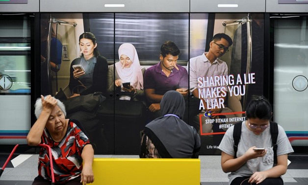 Commuters sit in front of an advertisement discouraging the dissemination of fake news, at a train station in Kuala Lumpur, Malaysia March 28, 2018. REUTERS/Stringer