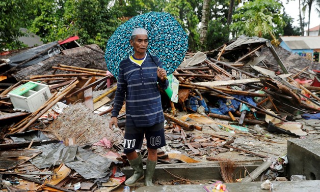 A man holding an umbrella walks through the debris of his damaged house after a tsunami in Sumur, Banten province, Indonesia December 26, 2018. Jorge Silva, Reuters
