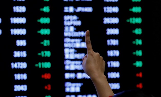 FILE PHOTO: A woman points to an electronic board showing stock prices as she poses in front of the board after the New Year opening ceremony at the Tokyo Stock Exchange (TSE), held to wish for the success of Japan's stock market, in Tokyo, Japan, January