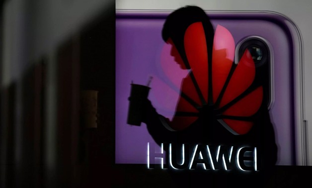 A man walking past a Huawei P20 smartphone advertisement is reflected in a glass door in front of a Huawei logo, at a shopping mall in Shanghai, China December 6, 2018. - Aly Song | Reuters