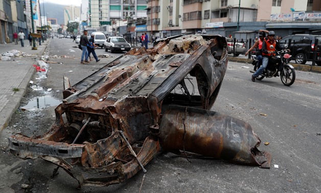 People walk close to a destroyed car in a street, after a protest in Caracas, Venezuela January 24, 2019. REUTERS/Carlos Garcia Rawlins
