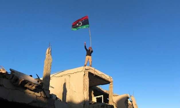 A fighter of Libyan forces allied with the U.N.-backed government waving a Libyan flag flashes victory sign as he stands atop the ruins of a house after forces finished clearing GhizaBahriya, the final district of the former Islamic State stronghold of Si