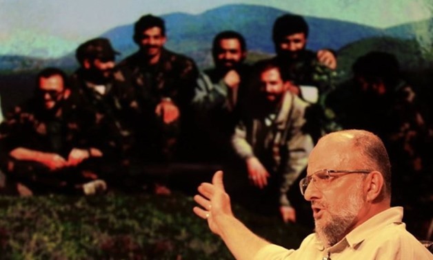 Iranian controversial conservative activist Saeed Ghasemi during an Interview with a photo in background showing him and his comrades during the Bosnian conflict in the early 1990s - Tasnim
