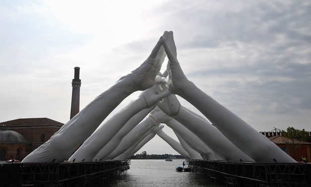 A general view shows the Italian artist Lorenzo Quinn's Building Bridges, a sculptural installation showing six pairs of arching hands creating a bridge over a Venetian waterway in the Arsenal former shipyard, in Venice on May 8, 2019. Tiziana Fabi / AFP 