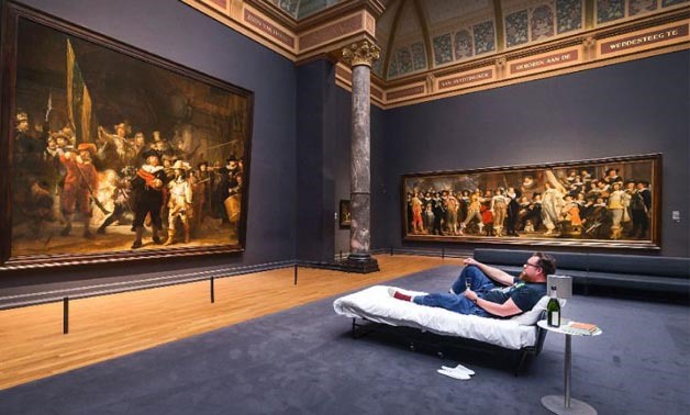 Lucky Stefan Kasper lying on a bed in front of the painting The Night Watch  by Dutch painter Rembrandt at Amsterdam's Rijksmuseum  - AFP