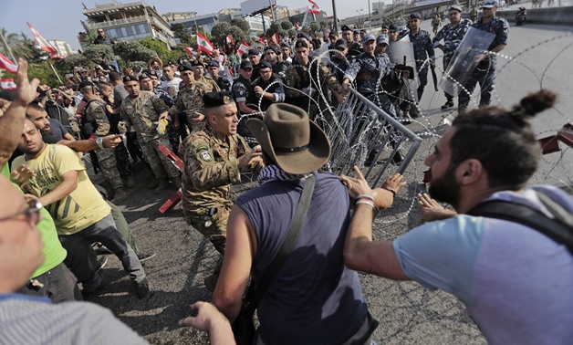 Lebanese demonstrators try to remove the barbed-wire and metal rail, placed by anti-riot police (background), on the road leading to the Presidential Palace in Baabda, on the eastern outskirts of Beirut on November 13, 2019. ANWAR AMRO / AFP