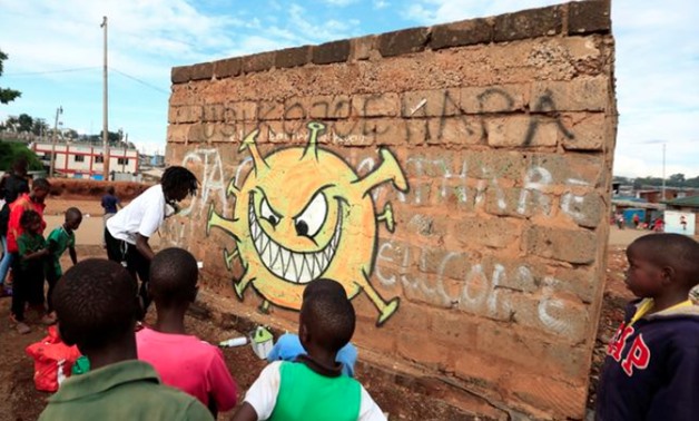 Children look on as Brian Musasia Wanyande, an artist from the Mathare Roots's youth group, paints an advocacy graffiti against the spread of the coronavirus disease (COVID-19), at the Mathare Valley slum, in Nairobi, Kenya April 19, 2020. REUTERS/Thomas 