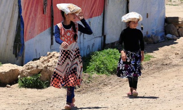 Syrian refugee girls carry stacks of bread on their heads, as Lebanon extends a lockdown to combat the spread of the coronavirus disease (COVID-19) at a Syrian refugee camp in the Bekaa valley, Lebanon May 7, 2020. REUTERS/Ali Hashisho
