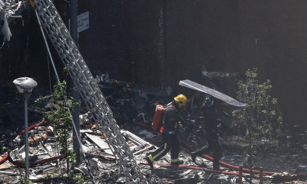 A police officer holds a riot shield over a firefighter at a tower block severely damaged by a serious fire, in north Kensington, West London, Britain June 14, 2017 -
 REUTERS