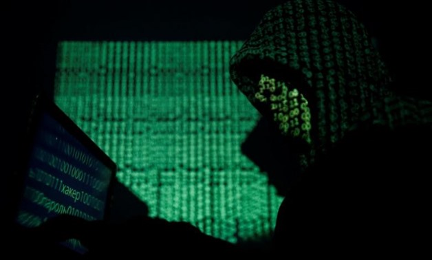 A hooded man holds a laptop computer as cyber code is projected on him in this illustration picture taken on May 13, 2017. REUTERS/Kacper Pempel/Illustration
