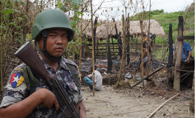 A Myanmar border guard police officer stands guard in front of the remains of a house burned down in a clash between suspected militants and security forces in Tin May village, Buthidaung township, northern Rakhine state, Myanmar - REUTERS