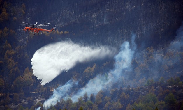 A firefighting helicopter makes a water drop as a wildfire is being contained after four days near the village of Kapandriti, north of Athens - REUTERS