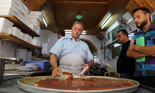 A Palestinian man serves knafa, a sweet semolina and cheese pastry, at al Aqsa sweet shop in the historic covered market of Nablus in the West Bank August 10, 2017.
Ammar Awad