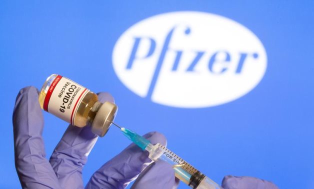 FILE: A woman holds a small bottle labeled with a "Coronavirus COVID-19 Vaccine" sticker and a medical syringe in front of displayed Pfizer logo in this illustration taken, October 30, 2020 - Reuters