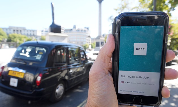 A photo illustration a London taxi passing as the Uber app logo is displayed on a mobile telephone, as it is held up for a posed photograph in central London -  REUTERS/Toby Melville