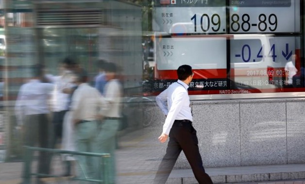 People walk past an electronic board showing exchange rate between Japanese Yen and U.S. Dollar outside a brokerage at a business district in Tokyo, Japan August 9, 2017. REUTERS/Kim Kyung-Hoon