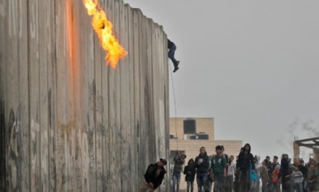© AFP | Palestinian protesters throw a Molotov cocktail and stones towards Israeli forces on the other side of a barrier at the Qalandia checkpoint in the occupied West Bank
