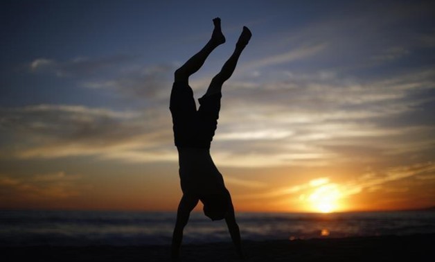 A man does a handstand as the sun sets over the Pacific Ocean on the beach in Santa Monica, California October 3, 2014. REUTERS/Lucy Nicholson