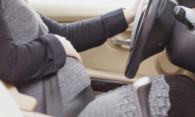 A pregnant women buckling her seat belt correctly across the center of her chest – Creative Commons