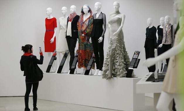 A visitor takes a photo of a display of dresses in the "Women Fashion Power exhibition at the Design Museum in London November 4, 2014 - REUTERS/Suzanne Plunkett