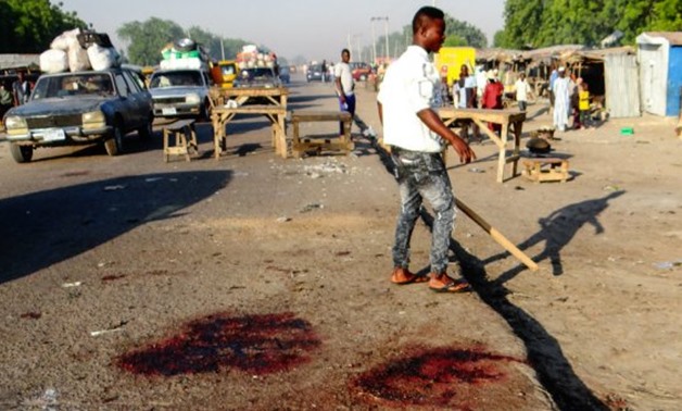 A man stands with his back to the blood stained scene of three suicide bomb blasts that left 13 people dead in Maiduguri, northeast Nigeria, on October 23, 2017.