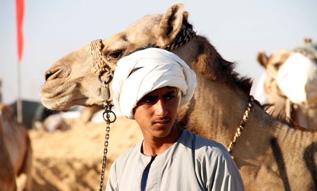 A young man stands next to his camel during the festival on March 13, 2018 – Mohamed Awad
