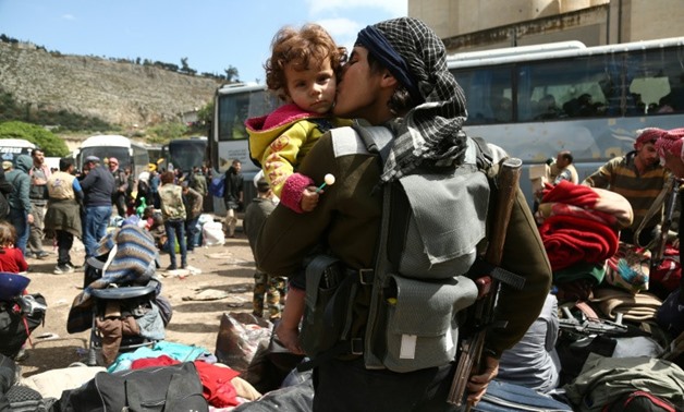 A rebel fighter from Eastern Ghouta, holds his weapon as he kisses a child after arriving in Qalaat al-Madiq, some 45 kilometres northwest of the central city of Hama, on March 30, 2018, following the ongoing evacuation deals
- AFP