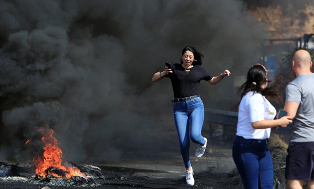A bystander makes her way through burning tires blocking off a main road leading from southern Lebanon to Beirut, during a protest targeting the government over an economic crisis, at Barja area, Lebanon, October 18, 2019. REUTERS/Ali Hashisho