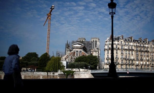 FILE PHOTO: A woman looks at Notre-Dame de Paris Cathedral, which was damaged in a devastating fire one year ago, as restoration work resumes slowly after an interruption due to the lockdown imposed to slow the rate of the coronavirus disease (COVID-19) i